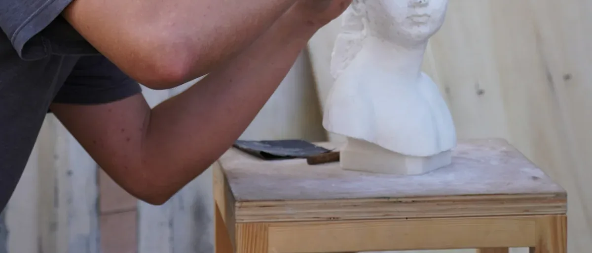 Mains d'un sculpteur taillant un buste blanc sur son socle, geste de l'atelier